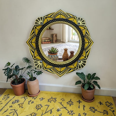 Decorative round mirror with yellow and black patterns on a wall above a yellow rug with plant decor.