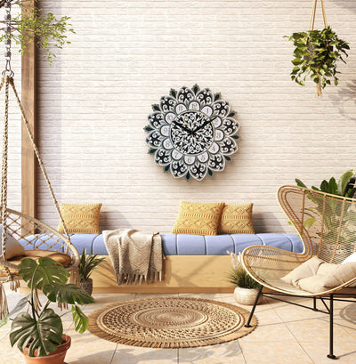 Decorative wall clock on a white brick wall with a couch, chair, and plants in a room.