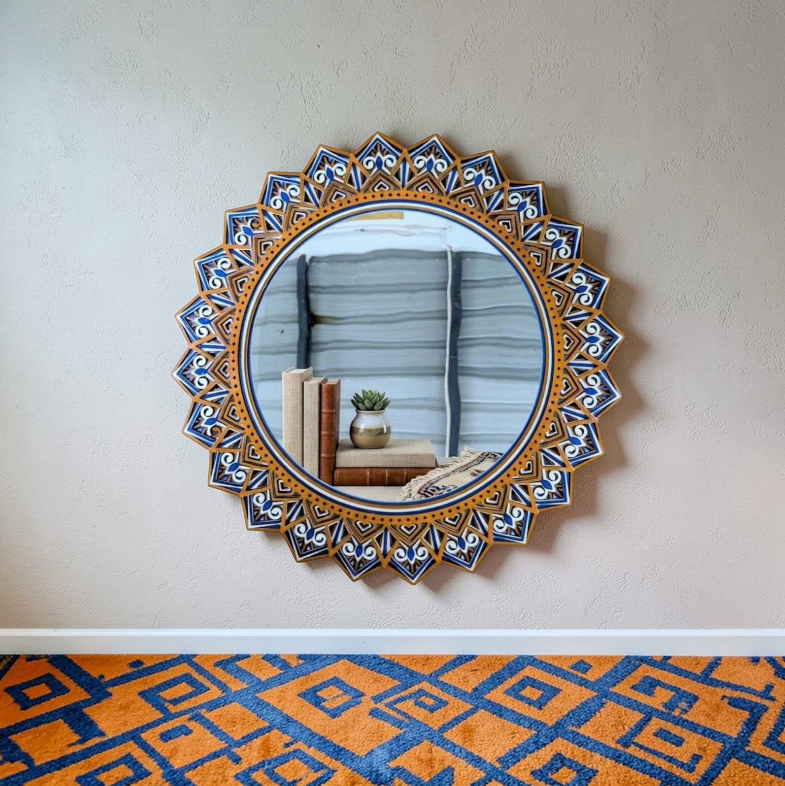 Decorative round mirror with intricate blue and gold frame on a plain wall.